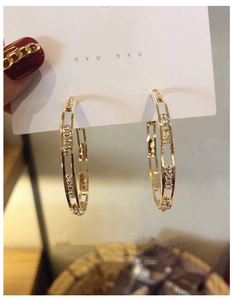 Detail of a C-shaped gold metal earring with embedded sparkling zircon stones