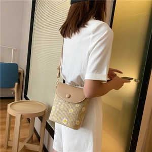 Detail of straw woven bucket bag with white daisy patterns and khaki PU leather strap