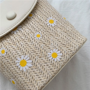 Detailed macro view of woven straw bucket bag featuring white daisy patterns and PU flap