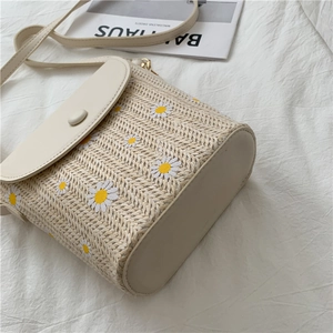 Close-up of beige woven bucket bag with white daisy embroidery on a soft fabric background