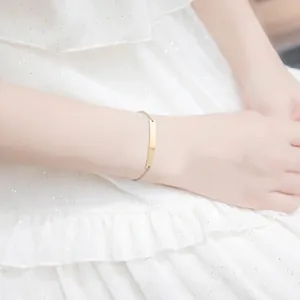Macro detail of a polished gold geometric bar bracelet on a woman wrist wearing white