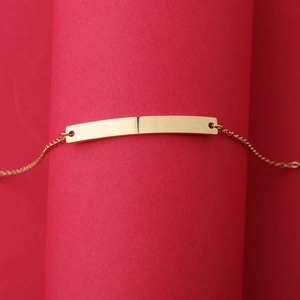 Macro detail of polished gold bar charm on minimalist adjustable stainless steel bracelet