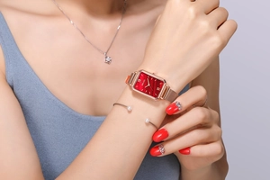 Detail of red rectangular dial watch with rose gold mesh band on woman's wrist