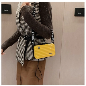 Close-up of yellow mini suitcase crossbody bag with Young lettered strap and stripe detail