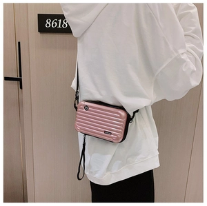 Close-up of pink hardshell mini suitcase crossbody bag with vertical stripe texture and logo