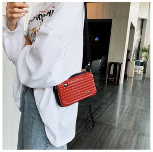 Red mini suitcase crossbody bag with hard shell texture and adjustable black strap