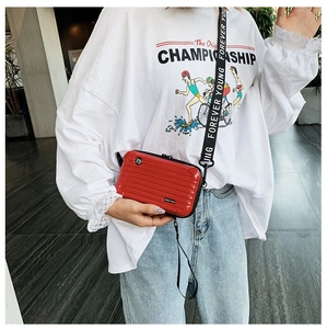 Glossy red mini suitcase crossbody bag with lettered wide strap on a female model