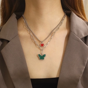 Double-layered silver necklace with red heart and green butterfly pendants on model
