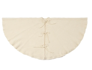 Close-up of cream knitted Christmas tree skirt with thick textures and delicate ribbon bows