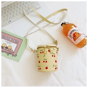 Detail of cream girls' bucket bag with cherry print and flower zipper on white fabric