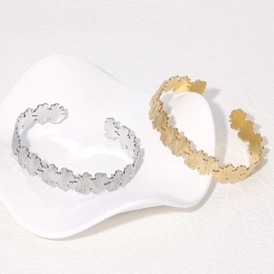 Gold and silver leaf-shaped stainless steel open bangles on a white ceramic dish