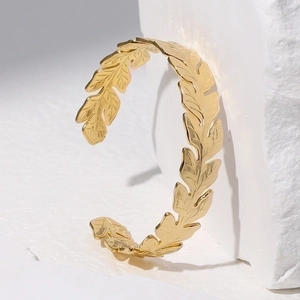 Detailed view of a gold leaf-shaped open cuff bracelet on a white textured stone surface
