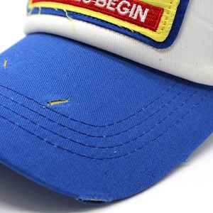 Close-up of distressed brim stitching and embroidered BEGIN patch on baseball cap