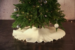 Detail of a creamy white knitted Christmas tree skirt with elegant wavy edges and soft texture