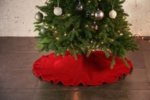 Detail view of red knitted Christmas tree skirt covering the base in a cozy setting