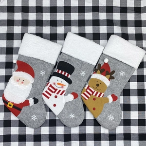 Three grey plush Christmas stockings featuring Santa, Snowman, and Reindeer on plaid background