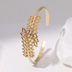 Detail of gold hollow leaf stainless steel bangle on white natural stone base