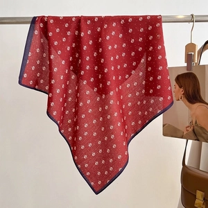 Detail of red square scarf with white leaf pattern and dark blue border on a hanger