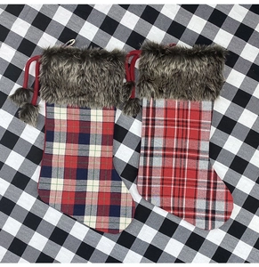 Flat lay detail of two plaid Christmas stockings with faux fur trim and red poms