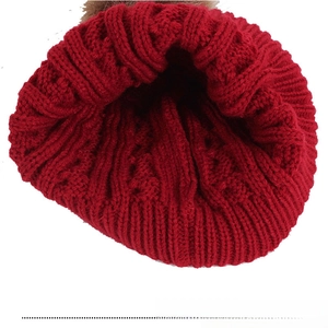 Detailed view of dark red cable knit beanie with fluffy brown faux fur pompom decoration