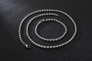 Detailed view of silver twisted stainless steel necklace and bracelet set on black texture