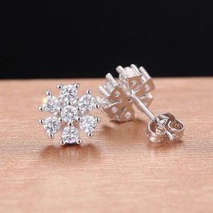 Elegant silver snowflake earrings with round clear gemstones on a textured surface