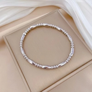 Polished silver titanium steel bangle with oval and round bead design on leather tray
