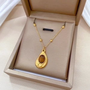 Gold titanium necklace with brown oval stone teardrop pendant in a beige gift box