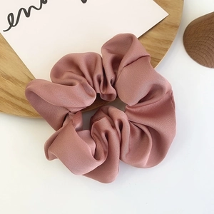 Detailed texture of silky satin scrunchie in dusty rose color on a wooden tray