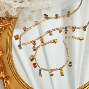 Elegant gold titanium bracelet with colorful zircon pendants on a vintage mirror tray