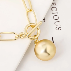 Detailed view of a gold ball pendant necklace with paperclip chain and toggle clasp