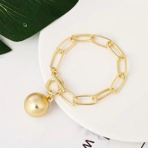 Detailed shot of golden link chain bracelet with toggle clasp and ball pendant on tray