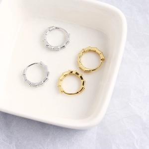 Macro view of gold and silver S925 sterling silver snake scale hoop earrings on ceramic dish