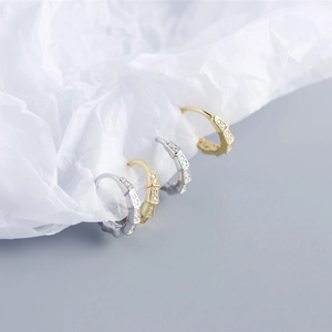 Macro shot of silver and gold hexagonal huggie earrings with cubic zirconia inlays