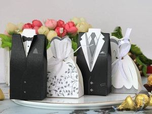 Detail of tuxedo and bridal gown wedding candy boxes with satin ribbons on a decorative plate