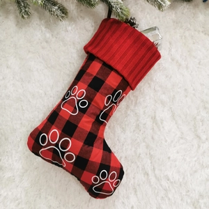 Detailed view of red black plaid Christmas stocking with paw print on plush white rug