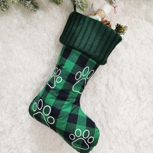 Detail of green plaid pet Christmas stocking with white paw print on plush background