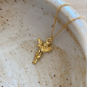 Detailed view of a mini golden angel pendant on a fine chain over ceramic decor