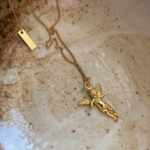 Detailed close-up of a gold angel pendant necklace in a ceramic speckled bowl