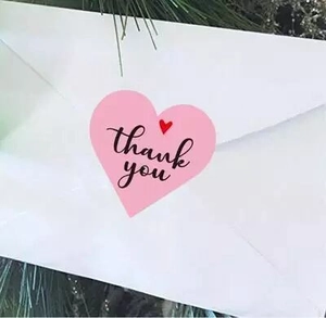 Pink heart-shaped thank you sticker used for sealing a white envelope in close-up