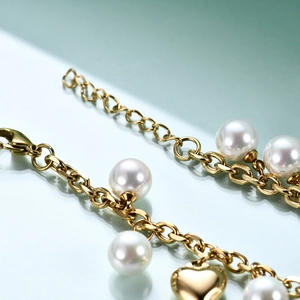 Close-up of gold chain bracelet featuring white pearls and a shiny heart pendant detail