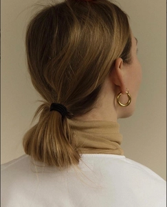 Detailed view of large gold-tone hoop earrings paired with a simple black hair tie