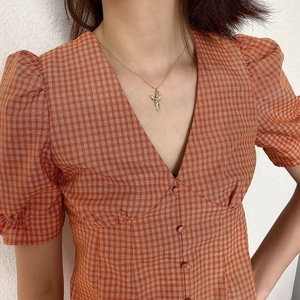 Detail shot of a minimalist gold angel pendant necklace worn over a red checkered dress