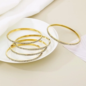 Set of 5 gold-plated stainless steel bangles with sparkling crystals on silk background