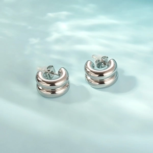 Polished silver two-tone C-shape hoop earrings on a light blue water ripple background