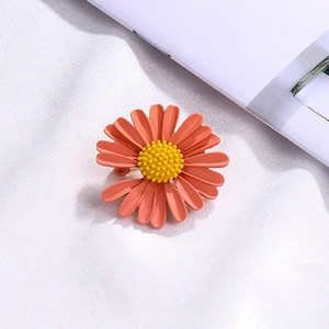 Detail of coral enamel daisy brooch with yellow center on white soft fabric