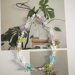 Close-up of handmade phone charm featuring transparent colorful resin butterflies and pearls
