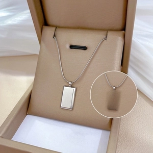 Macro view of silver rectangular pendant necklace with GOLD engraving in beige jewelry box