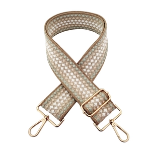 Detail of adjustable woven bag strap with beige and green wave patterns and gold buckles