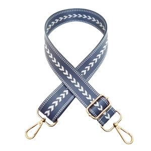 Macro detail of blue embroidered nylon bag strap with gold lobster clasps and buckle